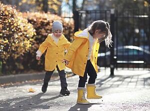 Two children in bright yellow raincoats and wellies playing on a sunny autumn day