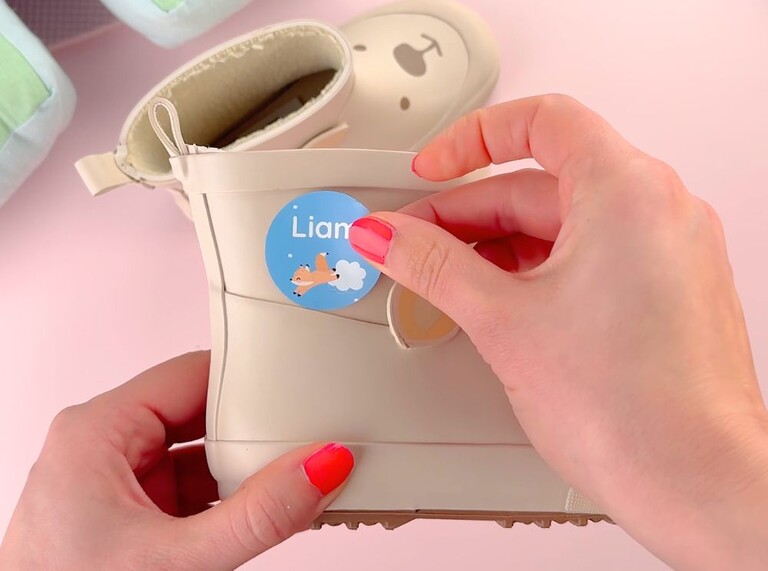 Applying a round blue name label with a fox design to a beige children's boot