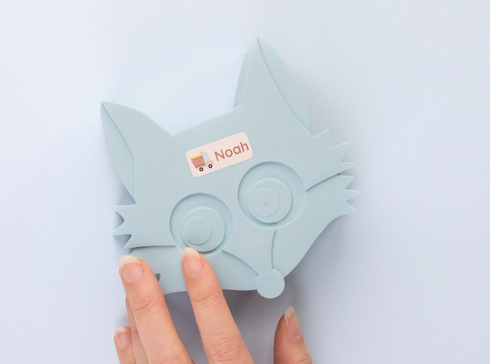 Personalised name label with a truck design attached to a light blue fox-shaped container