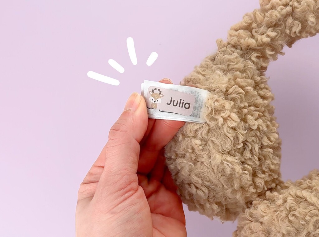 Hand holding a name label with a baby deer design, attached to a warm winter ear cover