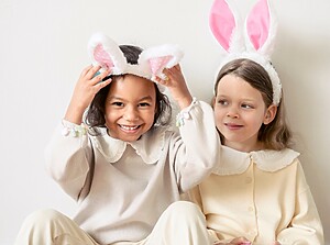 Two preschool children wearing bunny ear headbands, smiling and sitting together