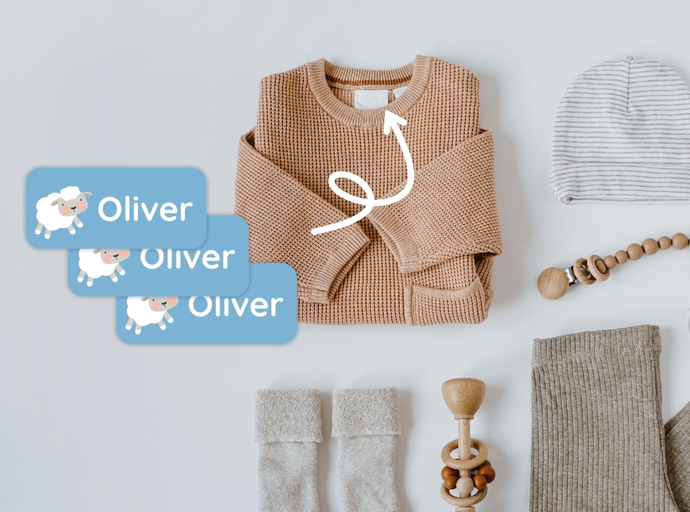 Flat lay of neutral baby clothes and accessories with blue name labels featuring a sheep and the name oliver