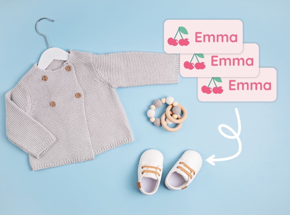 Flat lay of baby clothes and shoes with pink name labels featuring cherries and the name emma
