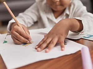 Preschool child drawing with a pencil on white paper at a table