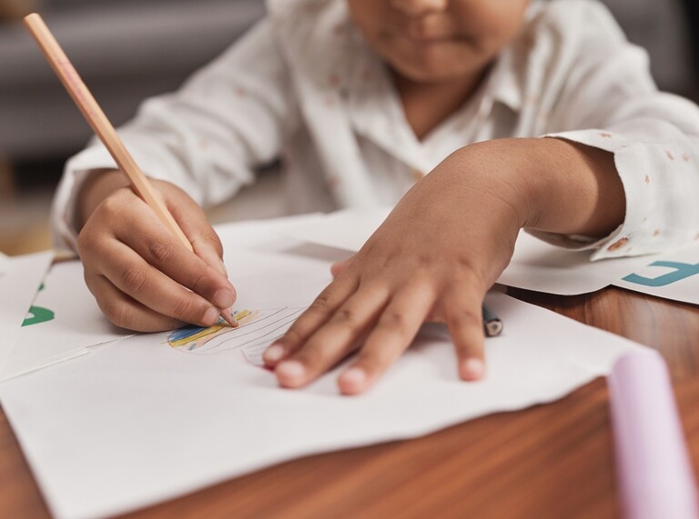 Preschool child drawing with a pencil on white paper at a table