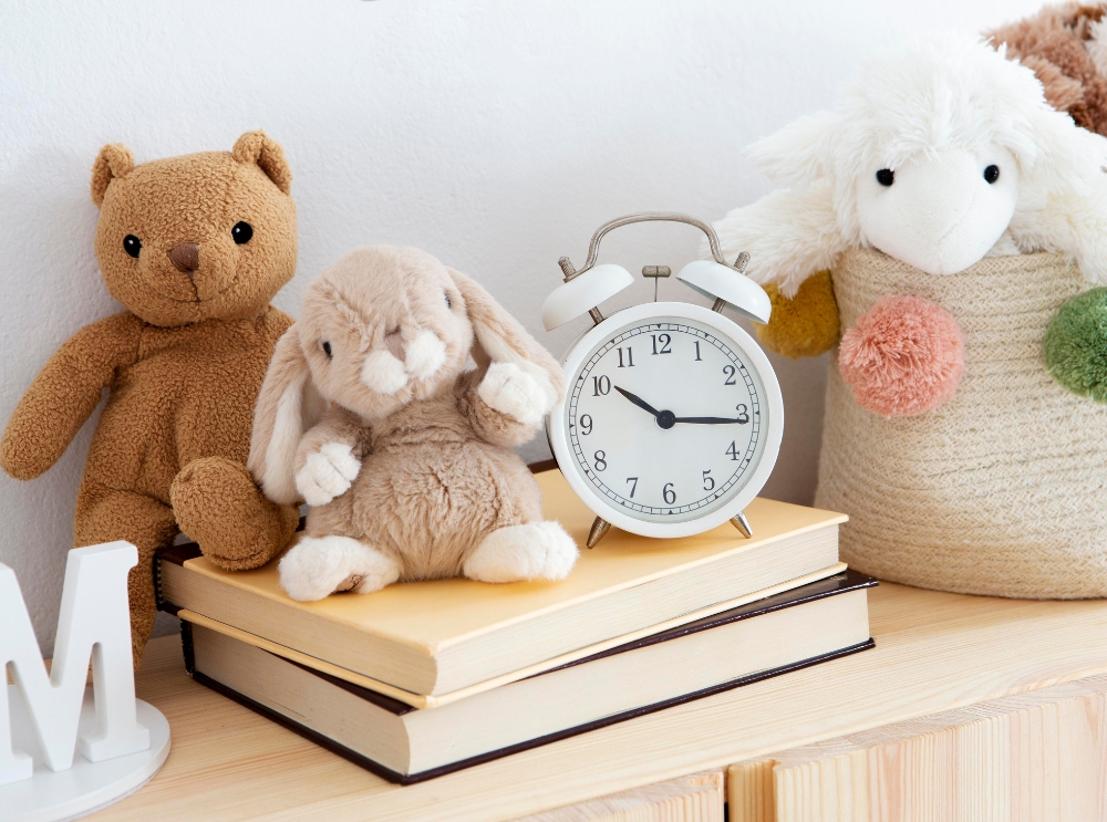 Stuffed animals and a white alarm clock on top of books in a cosy nursery setting