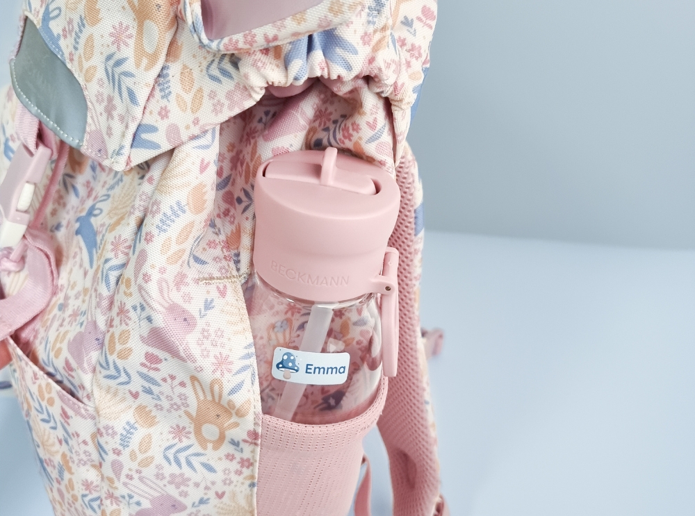 How to choose the right backpack for your child 1 Close-up of a pink drinking bottle with a personalised name label tucked into the side pocket of a floral backpack