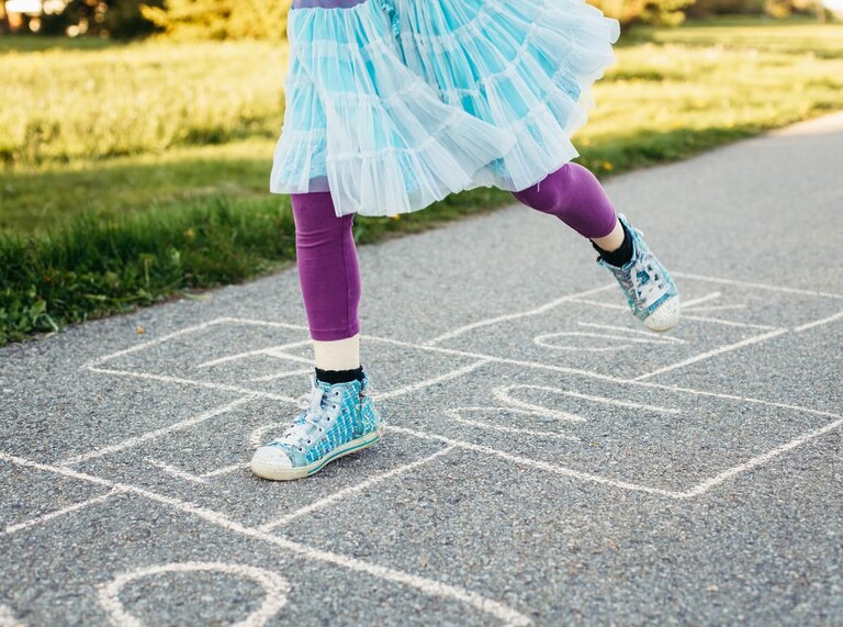 Child playing hopscotch on a sidewalk, wearing colorful sneakers.
