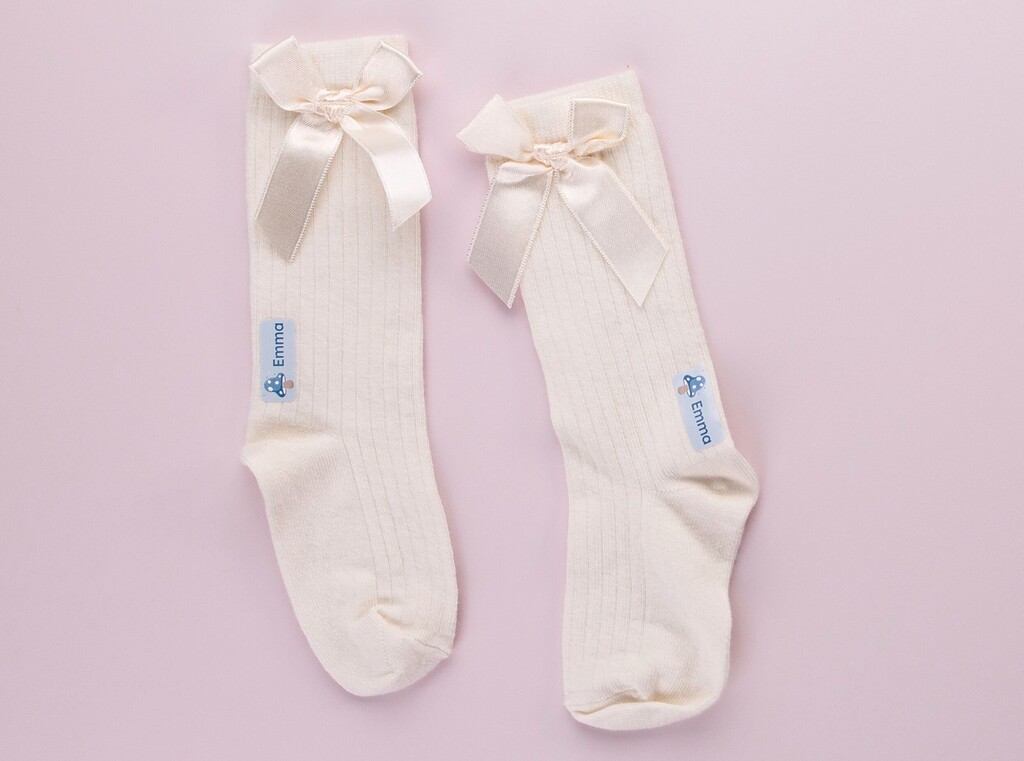 Two white woolen socks with an iron on-label with the name "emma" and a mushroom