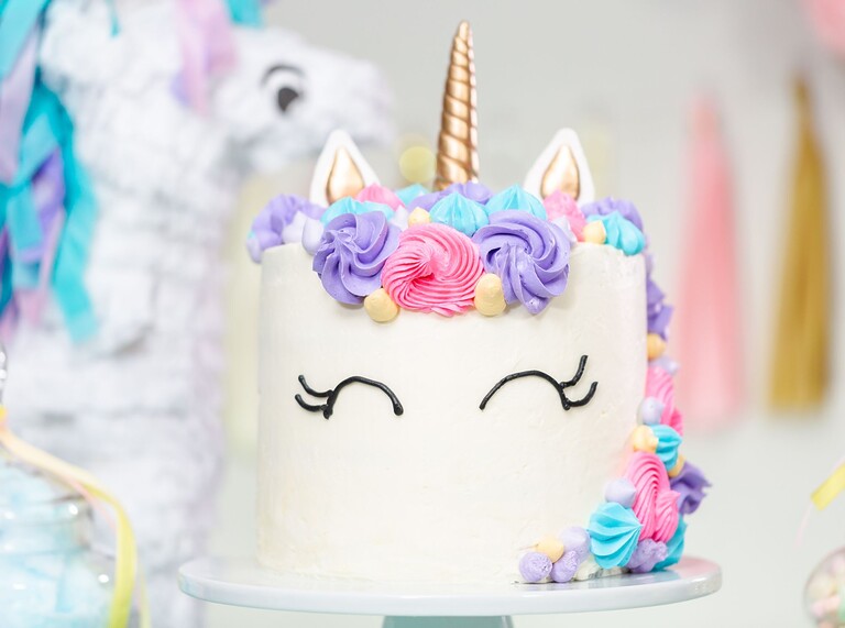 Unicorn cake with pastel frosting swirls, golden horn, and playful eye details.