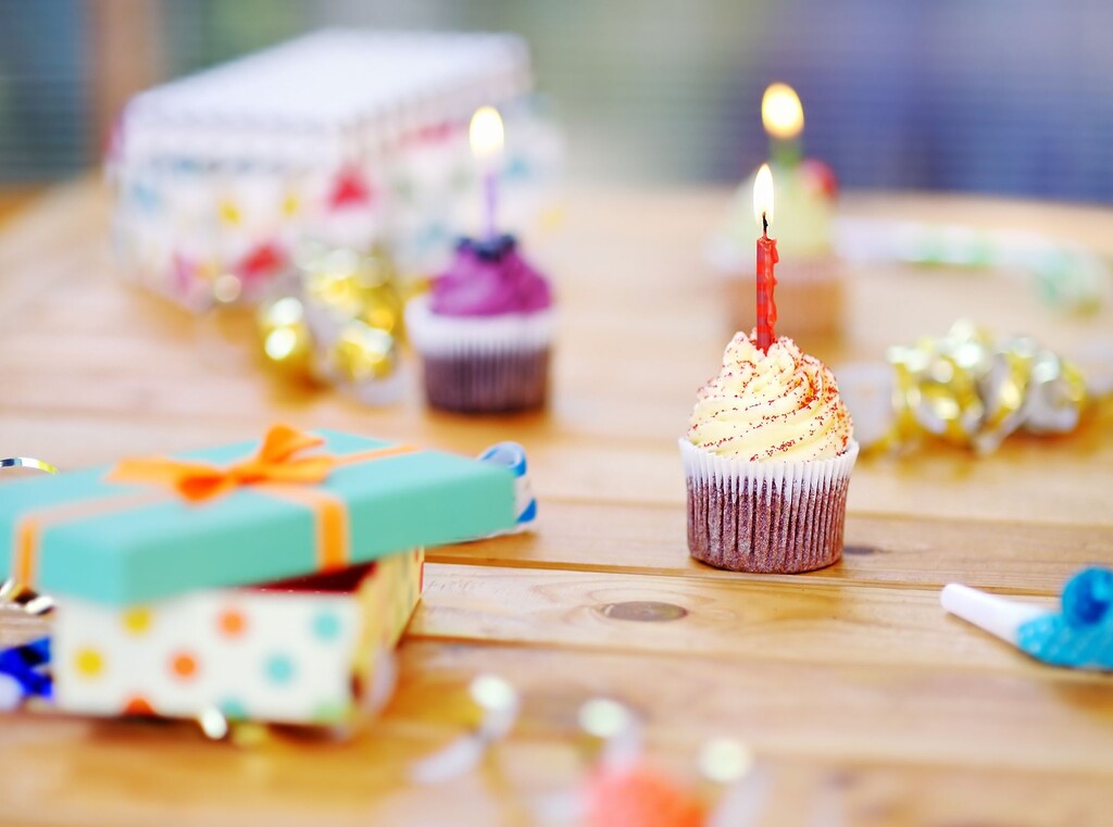 Cupcake with a burning birthday candle on a wooden table, next to wrapped presents and festive decor.