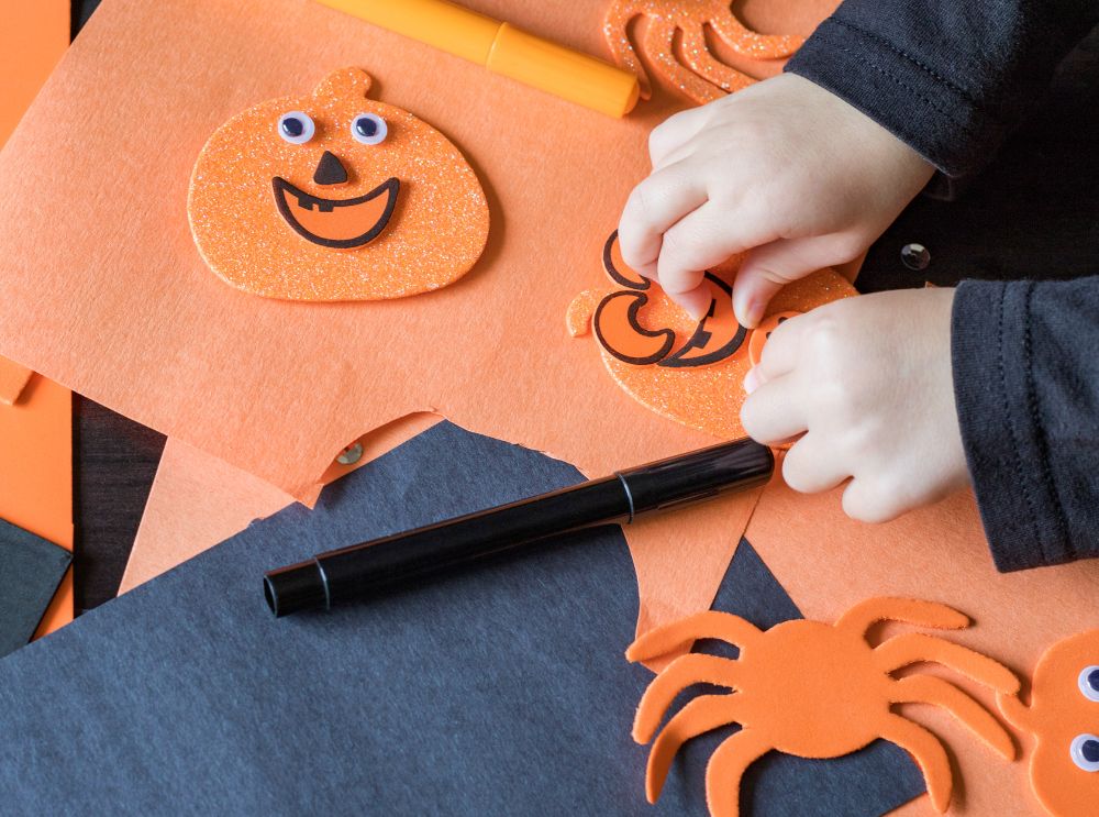 Child creating pumpkin decorations with orange and black paper