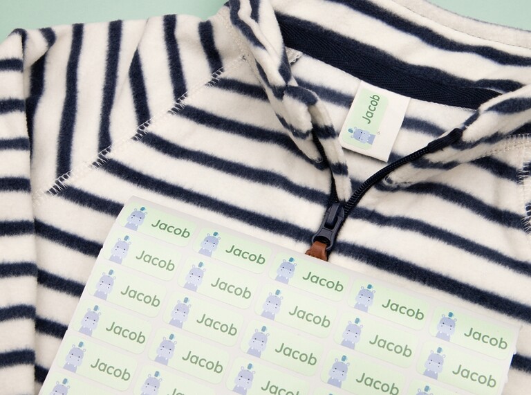Sheet of green namelabels with a hippo design placed on a striped kids' shirt