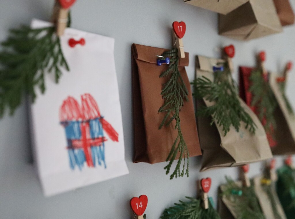 Close-up of homemade advent calendar bags hanging on a wall, decorated with drawings and small pine branches.