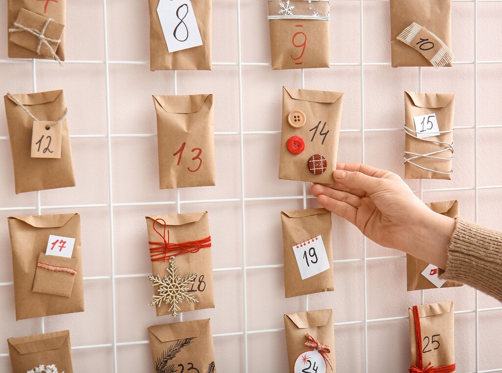 Hand reaching for a brown paper bag on a homemade advent calendar, with each bag numbered and decorated.