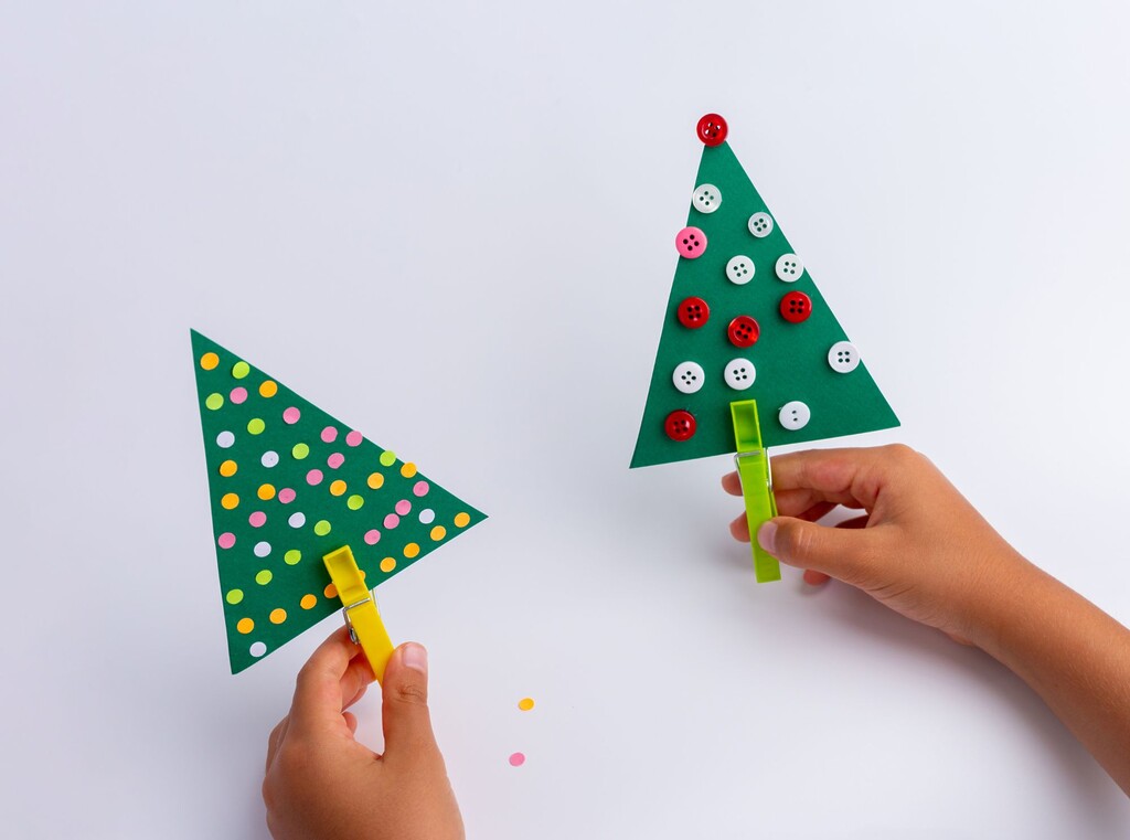 Children holding homemade paper christmas trees made from green cardboard, decorated with dots and buttons.
