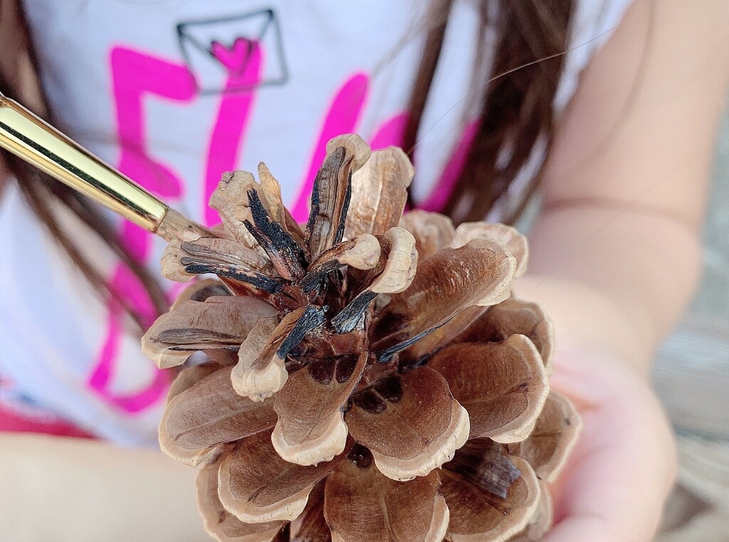 Child painting a pine cone for a fun christmas craft, adding colour and glitter.
