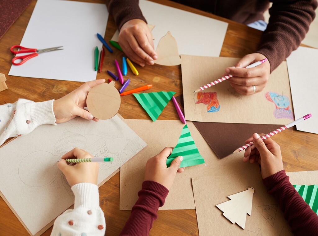 Children’s hands seen from above, gathered around a table making christmas crafts.