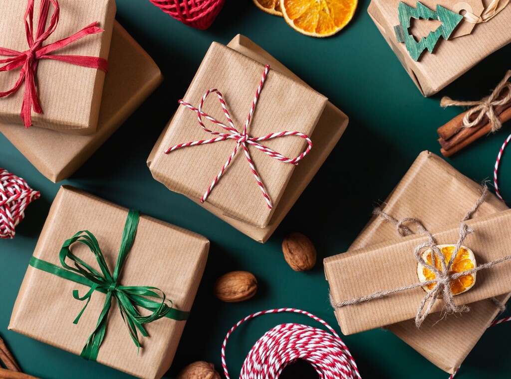 Flat lay of christmas presents wrapped in brown paper on a dark green background with dried orange and cinnamon.