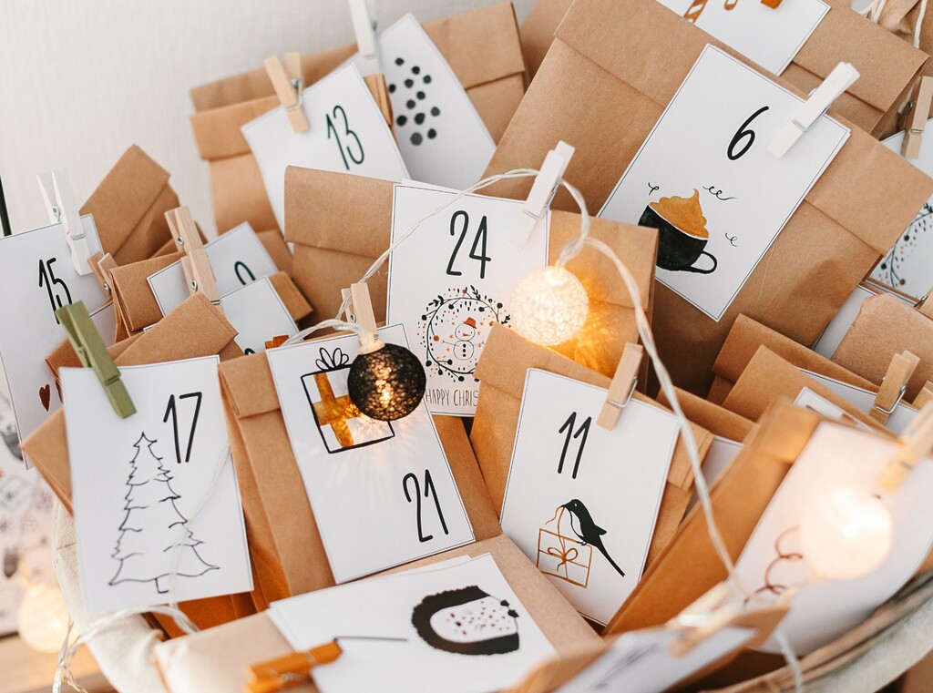 Close-up of a homemade advent calendar with brown paper bags, white numbered tags, wooden pegs and a decorative fairy light string.