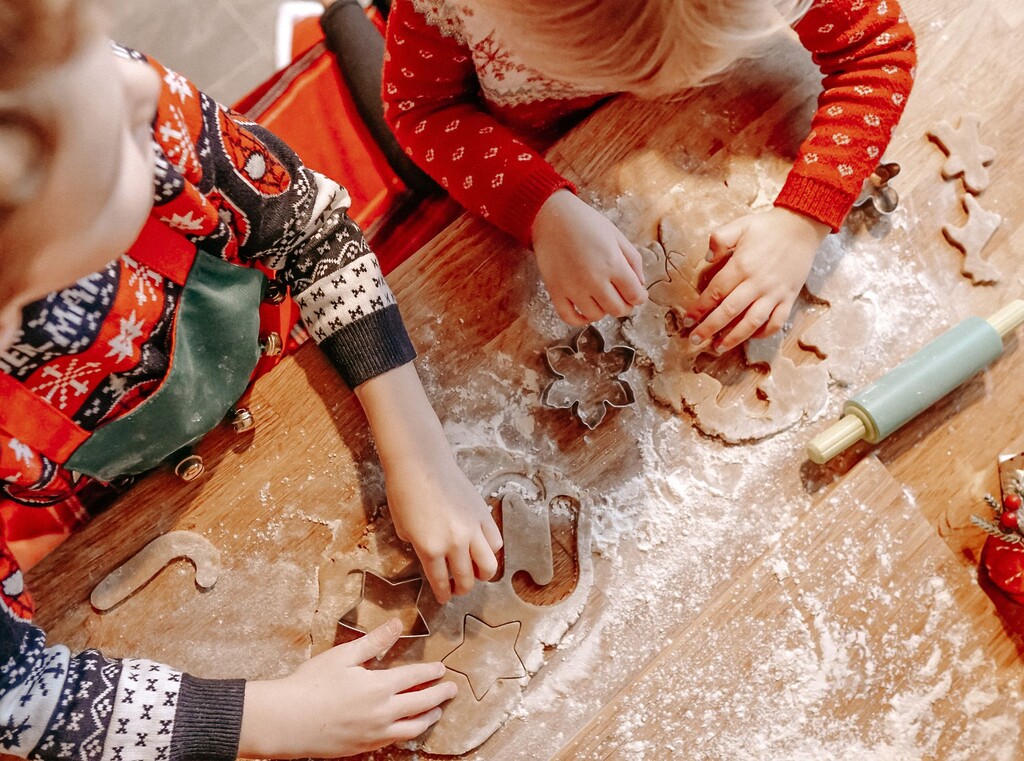 Children’s hands cutting out biscuit dough with festive cutters, seen from above.
