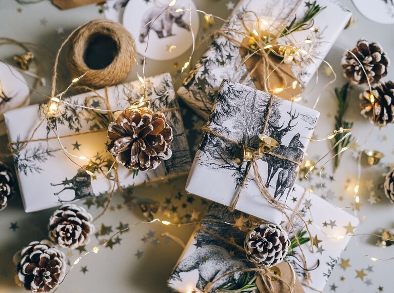 Festive flat lay of wrapped Christmas gifts with pinecones, twine, and warm fairy lights