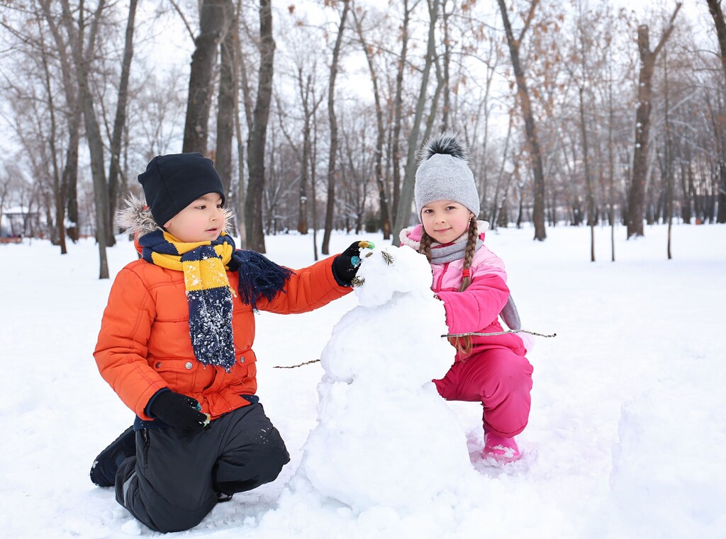 Snow much fun: the best winter activities for kids 1 Two children playing in the snow and building a snowman together in a winter park.