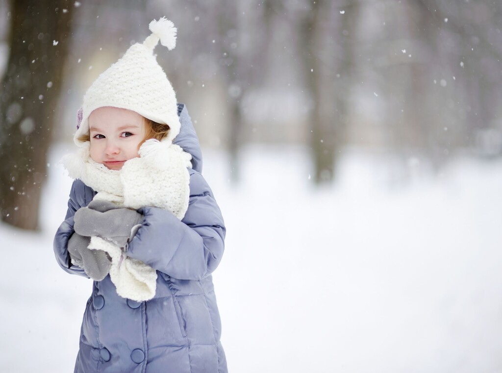 Toddler wrapped up in winter clothing standing in the snow.