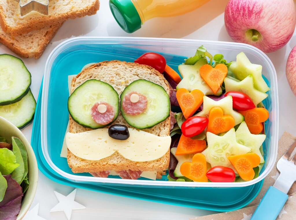 Fun children’s lunchbox with a face sandwich made from cucumber, cheese and salami, with star-shaped cucumber and carrot hearts.