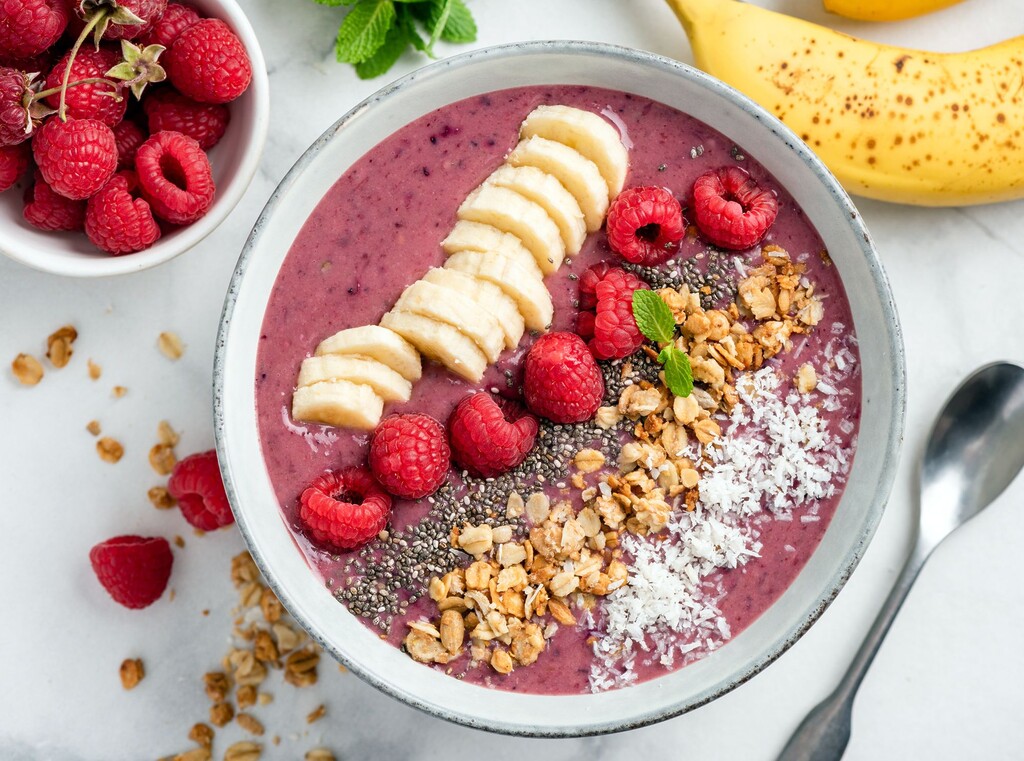 Berry smoothie bowl topped with banana slices, raspberries, granola, and chia seeds.