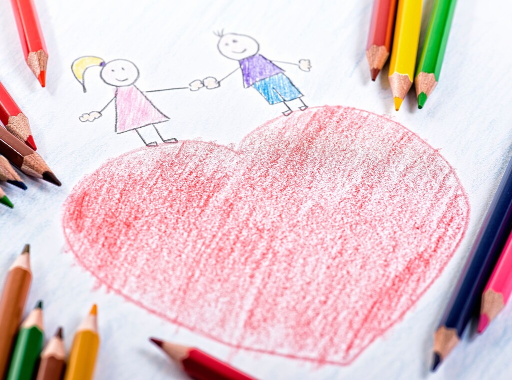 Child’s drawing of a large red heart with two stick figures holding hands, surrounded by colored pencils.