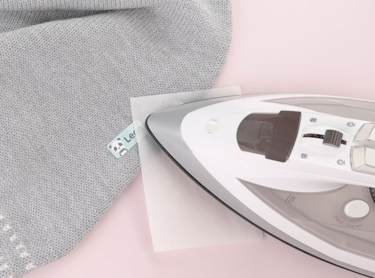 Iron pressing a personalised iron-on name label onto grey fabric