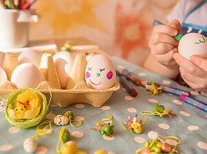 Small child drawing on an egg with a marker pen at the kitchen table