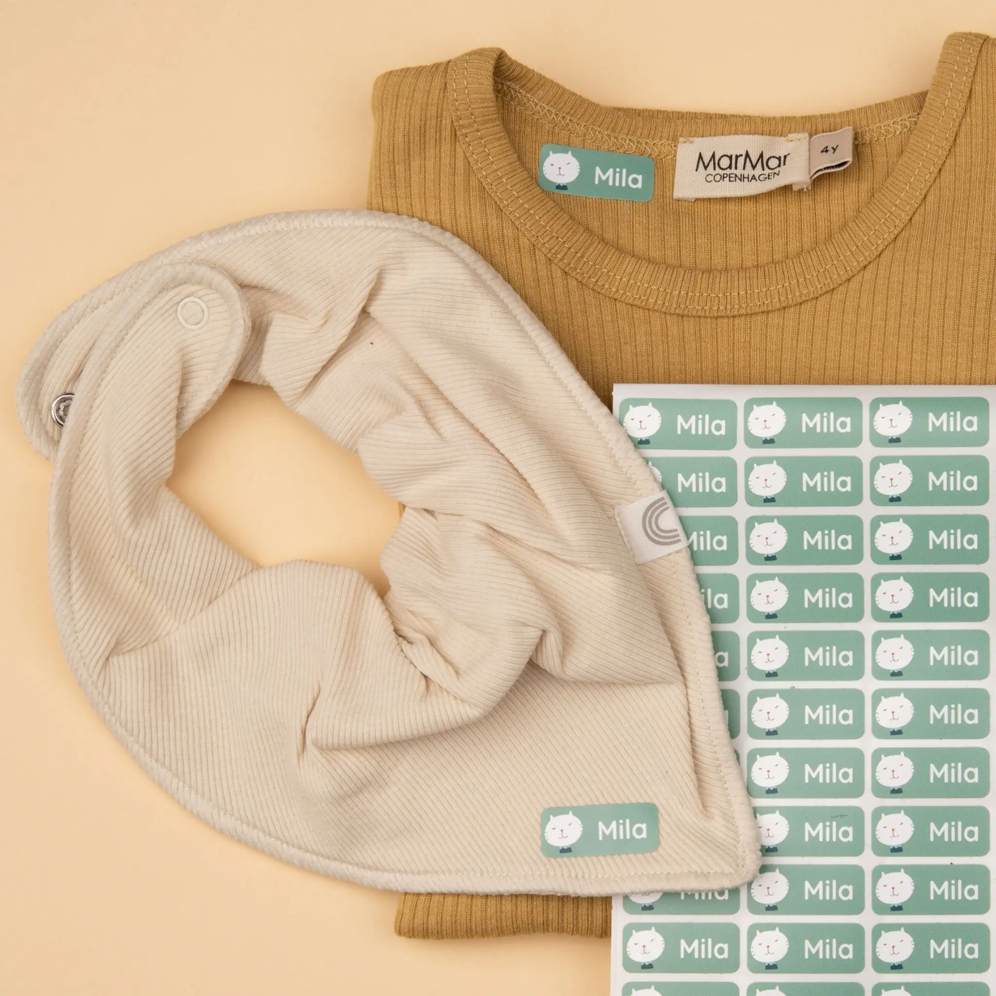 Personalized iron-on labels with a cat and the name "Mila" on clothing items and on a label sheet