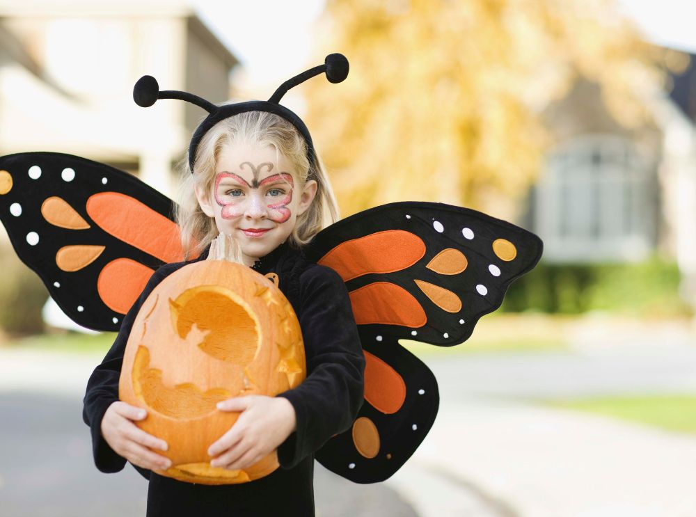 Girl in a butterfly costume holding a carved pumpkin