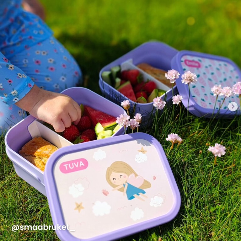girl sitting in the grass with a purple lunchbox