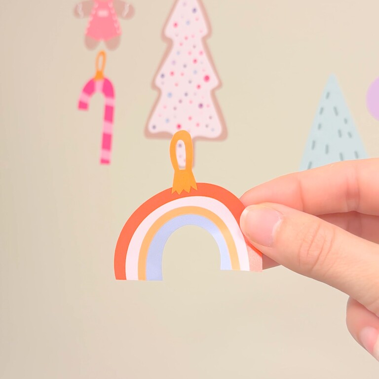 Holly jolly wall stickers - a hand holding one of the decoration elements shaped like a rainbow