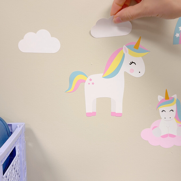 Wall stickers with unicorn, rainbows and flowers being placed on a wall