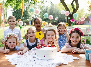 Children gathered around a birthday cake at an outdoor birthday party