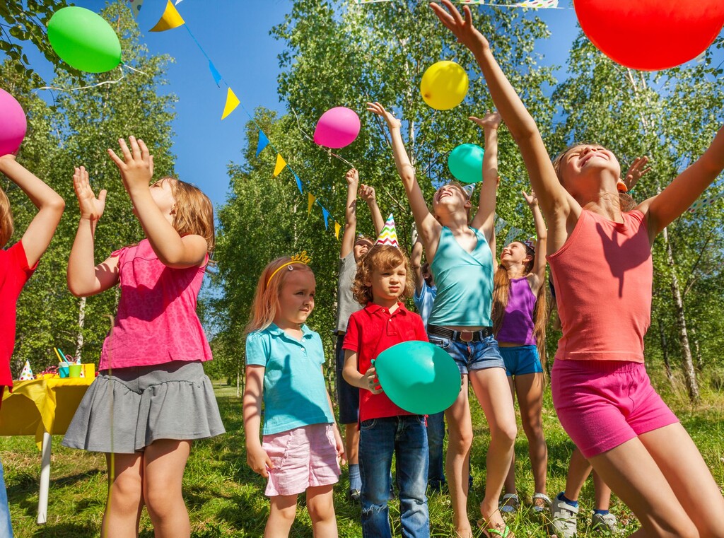 Outdoor birthday party ideas: how to plan a fun and easy celebration 2 Children throwing colourful balloons into the air at an outdoor birthday party